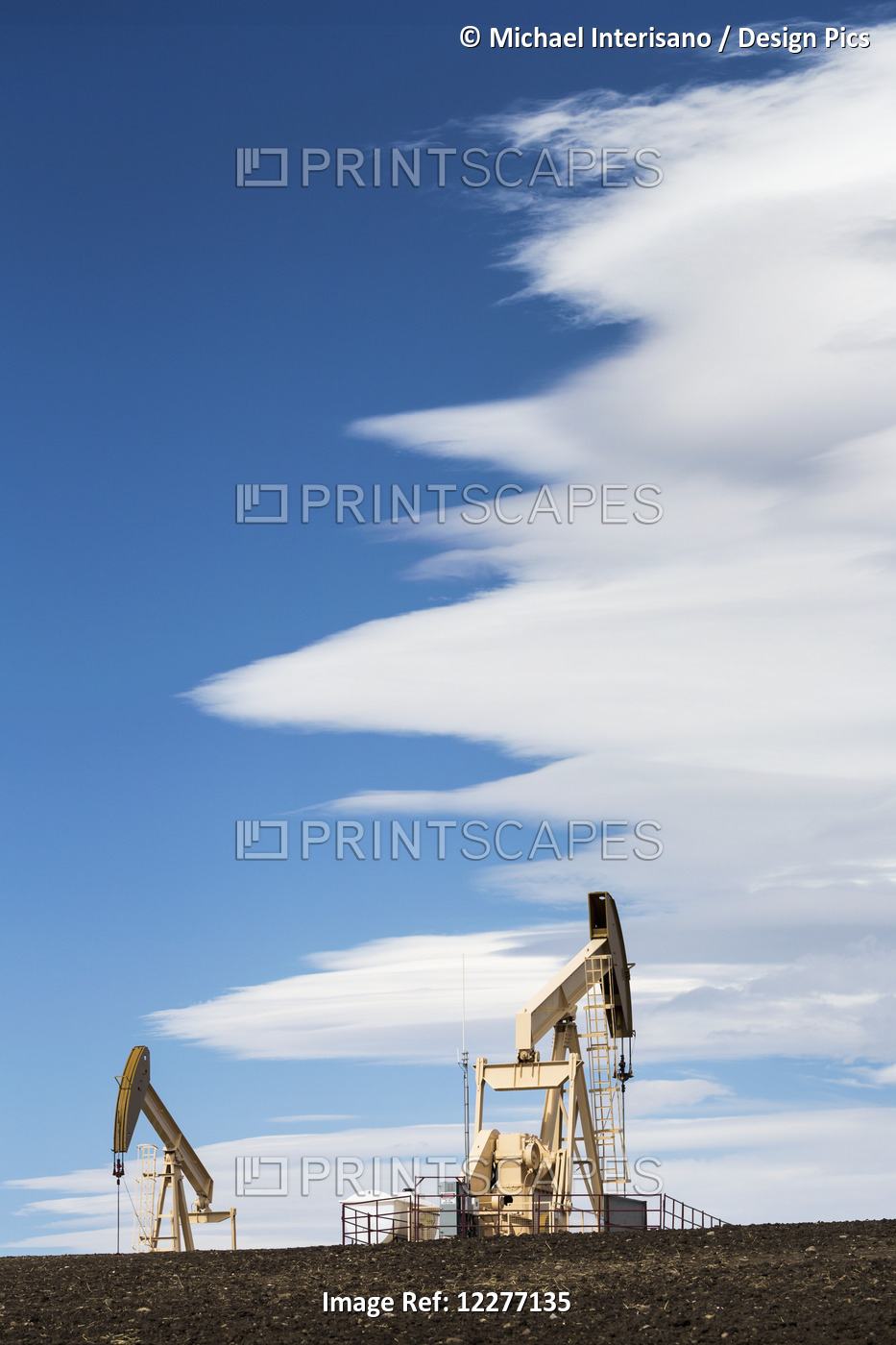 Two Pumpjacks On A Hill With Dramatic Clouds In The Blue Sky; Alberta, Canada