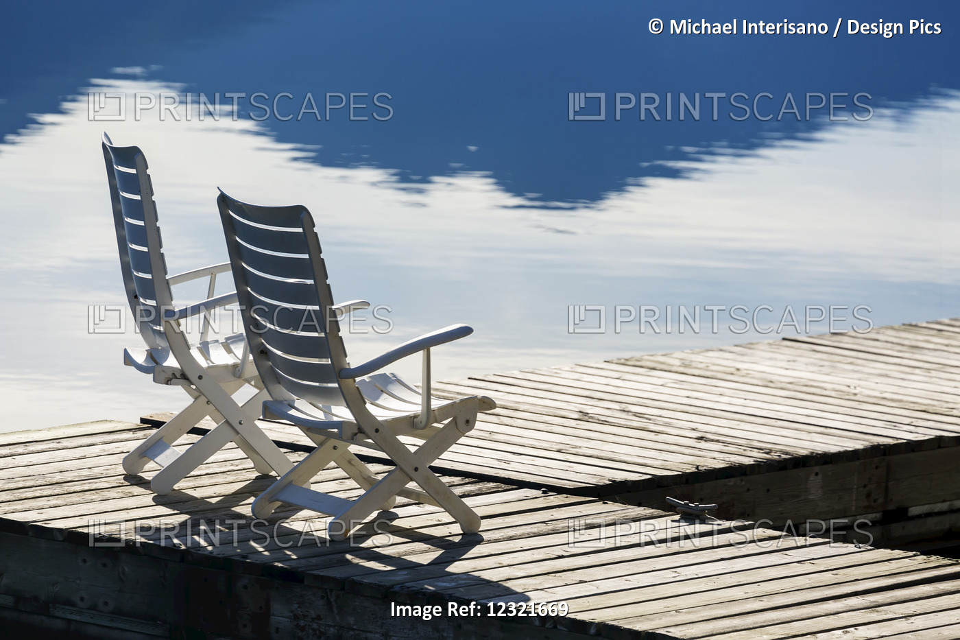 Two White Wooden Deck Chairs On Wooden Boat Dock Reflecting In The Water; ...